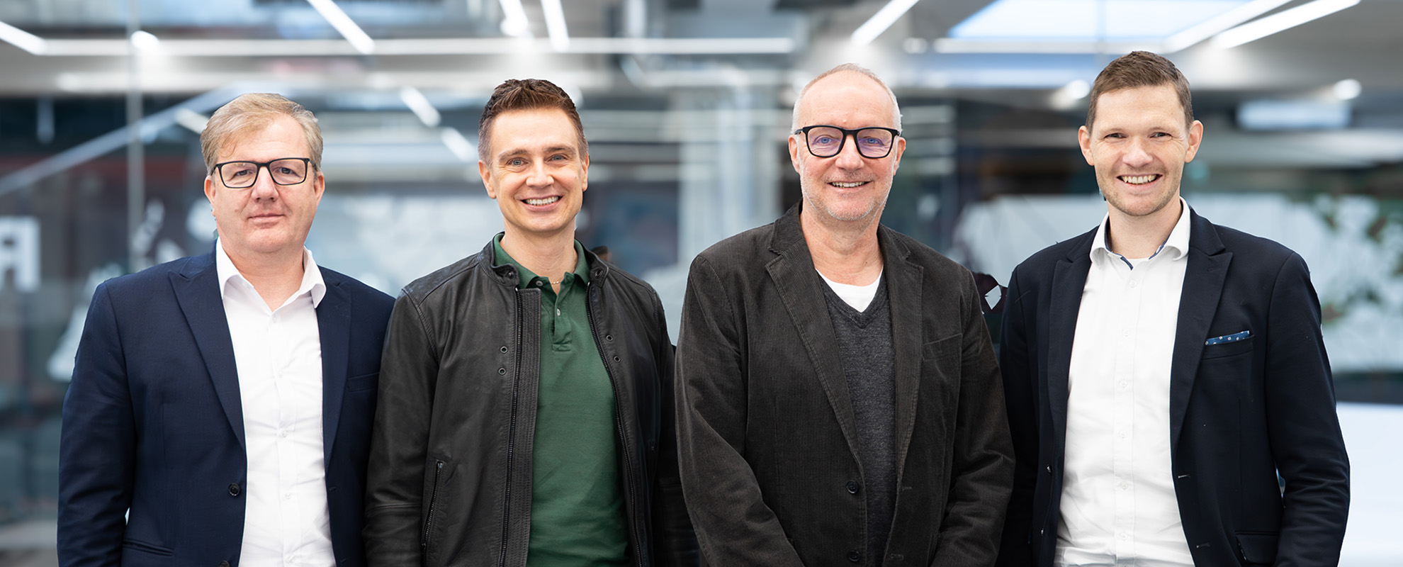 vier Männer im Anzug lächeln in die Kamera